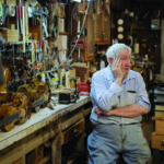Master Artist Jean Horner sits near a display of his fiddles in his shop in Westel, TN.