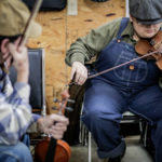Fiddler Michael DeFosche listens as apprentice Trenton Caruthers works out a tune they are practicing, on a Saturday morning at the Highway 111 Flea Market, in Cookeville, in December 2017.