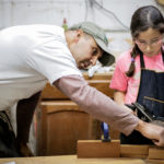 Manuel Delgado instructs Ava Delgado, apprentice, on the proper technique for planing what will become the neck of her custom mandolin. Ava represents the fourth generation of luthiers in the Delgado family.