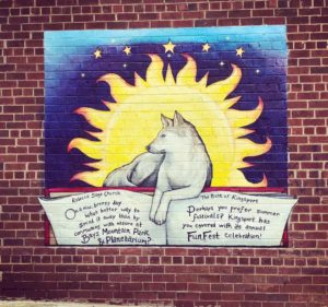 A mural on a brick wall depicts a white wolf in front of a large yellow sun with stars and a blue sky. A scroll below the wolf promotes Bays Mountain Park & Planetarium and Kingsport’s annual Fun Fest celebration.