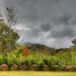 Dark storm clouds combined with round hay bales create a moody fall landscape.