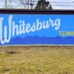 A mural on a blue wall features the word Whitesburg in large white script and Tennessee in yellow print, with painted leaves, a butterfly, a squirrel, and a bird on either side of the text.