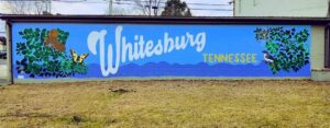 A mural on a blue wall features the word Whitesburg in large white script and Tennessee in yellow print, with painted leaves, a butterfly, a squirrel, and a bird on either side of the text.