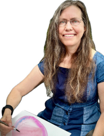 A woman with long brown hair and glasses, wearing a blue dress, smiles while holding a paintbrush and working on a watercolor painting with pink and purple hues. The background is plain white.