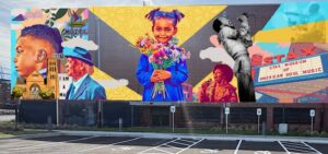 Colorful mural features a young girl holding flowers, portraits of men, a church, historic signs, and a dancing couple, highlighting civil rights and Memphis soul music themes. The mural is displayed on a brick wall above a parking lot.