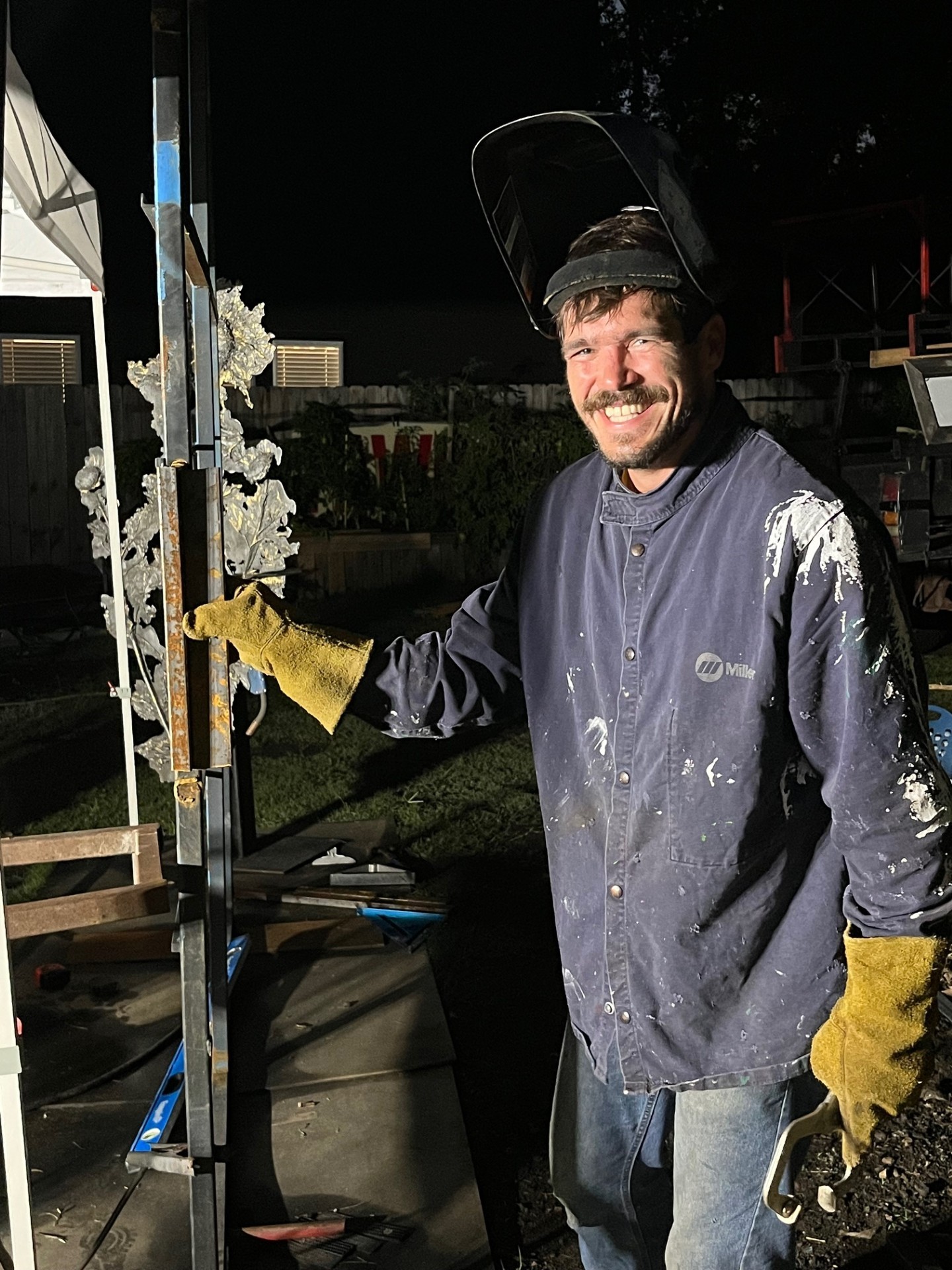 Robert Gregory in welding gear beside a metal sculpture in progress